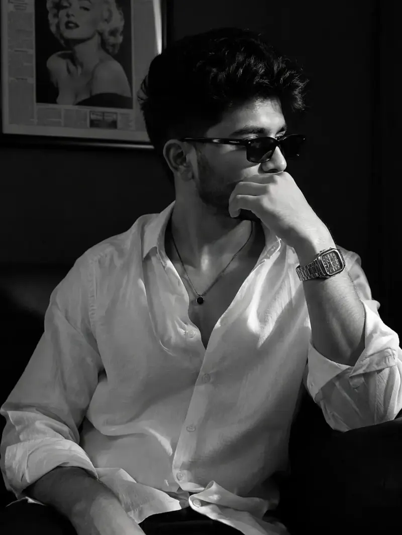 A cinematic black-and-white portrait of a stylish young person sitting in a… — GPT Image 2 prompt by @ChillaiKalan__